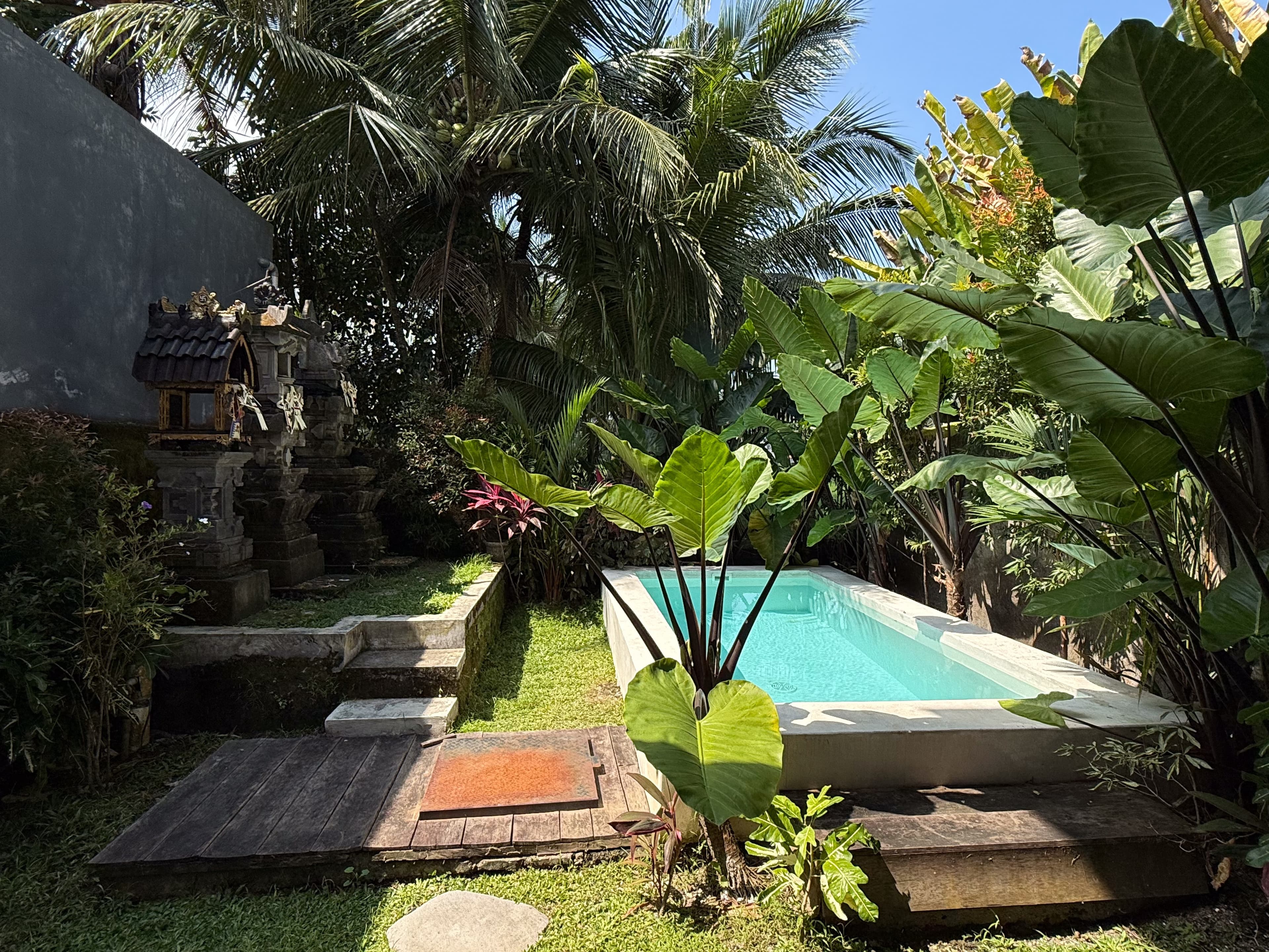 Garden and pool of an ATELIERO-managed Bali property, with a traditional Balinese shrine