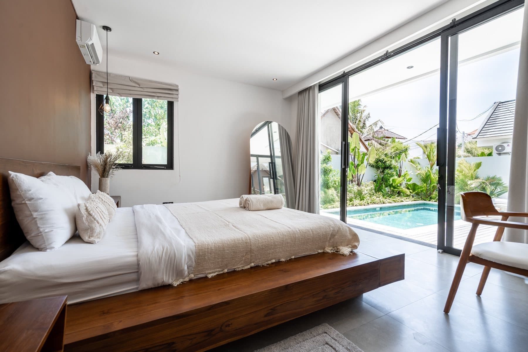 Furnished Bali villa bedroom with a wooden bed, light textiles and a pool view